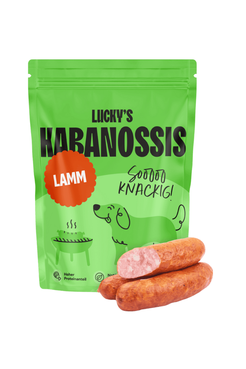 Luckys Kabanossi für Hunde, in schöner grüner Verpackung, mit einem Roten Sticker auf dem "Lamm" steht. davor liegen 3 Kabanossi, eins davon aufgeschnitten. 